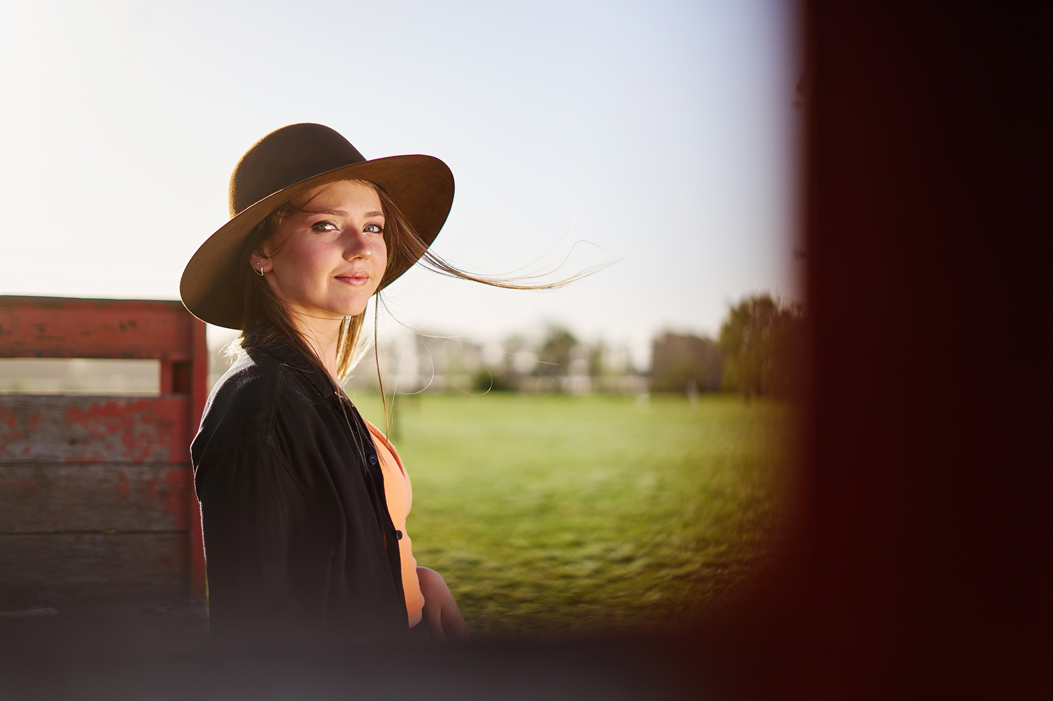 Retrato con sombrero de ala ancha en el campo, a contraluz, junto a una tranquera roja. Sesión en exteriores de DNX Estudio, Funes, Santa Fe.