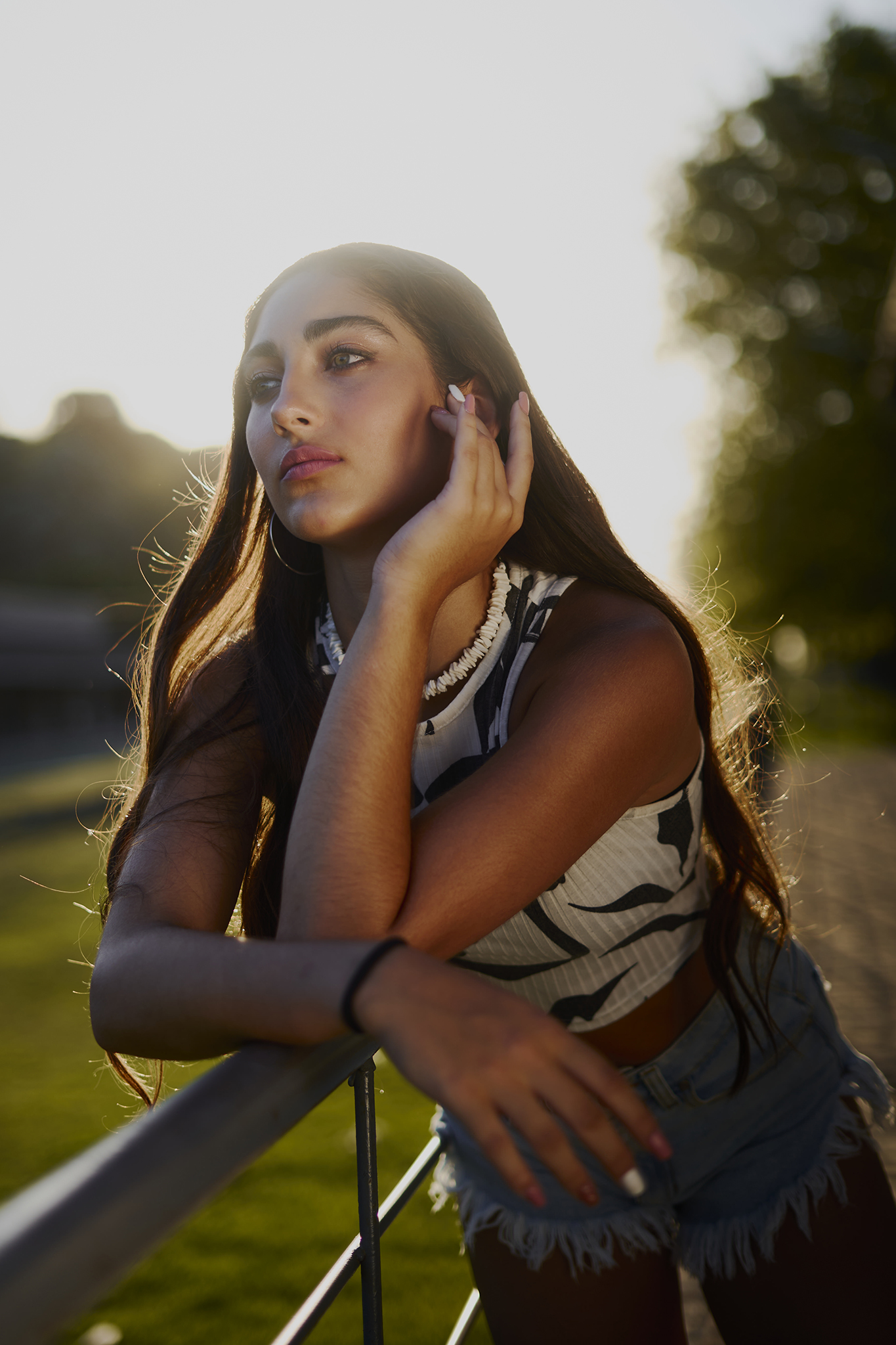 Retrato apoyada en una baranda con el sol dorado del atardecer de fondo. Book de quince en el parque, de DNX Estudio, Funes, Santa Fe.