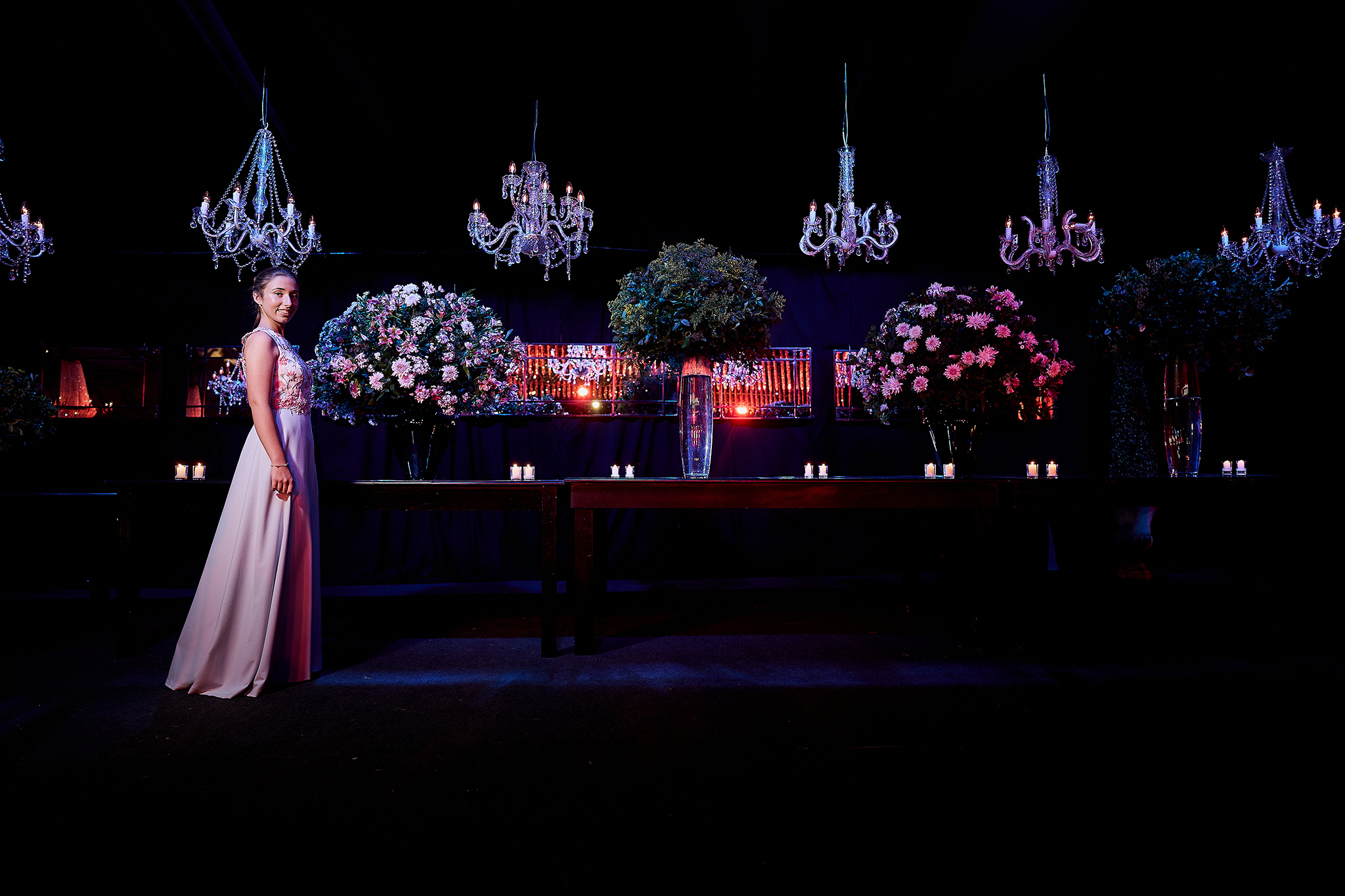 Chica de vestido largo junto a la mesa principal, con arañas de cristal y arreglos florales. Ambientación de fiesta de 15 por DNX Estudio, Funes.