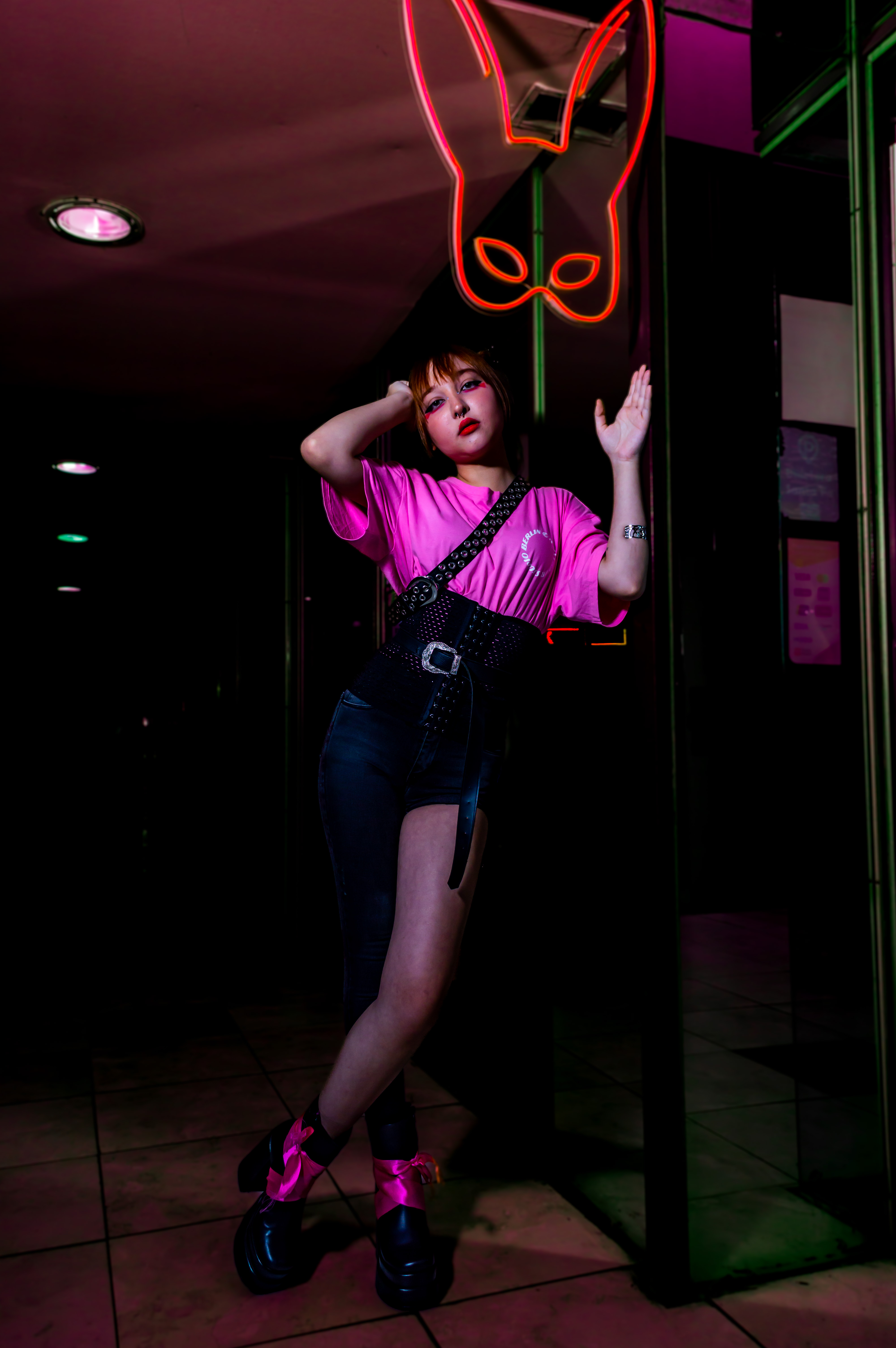 Retrato de una mujer con ropa negra y detalles rosa neón, posando bajo una luz roja. Rosario.
