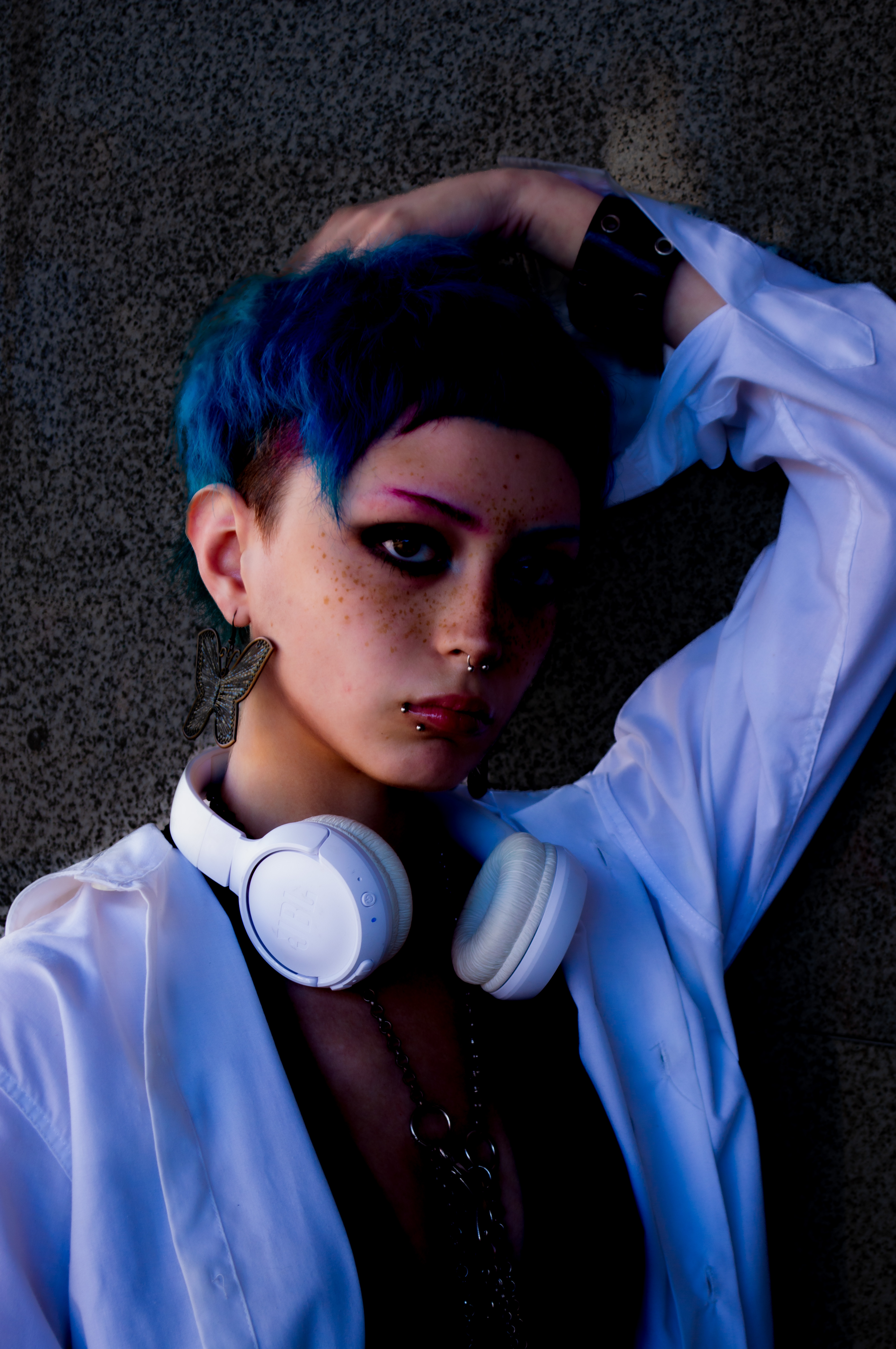 Una mujer con cabello azul oscuro, auriculares grandes y camisa clara posa con una mano sobre la cabeza. Rosario.