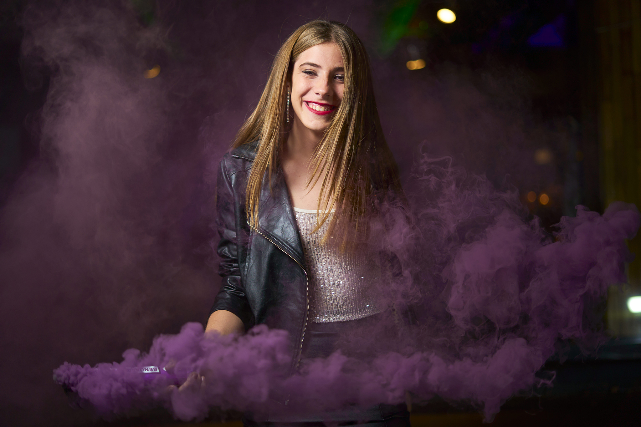 Sonrisa entre una nube de humo violeta, con campera de cuero, de noche. Sesión de 15 con humo de color de DNX Estudio, Funes, Rosario.