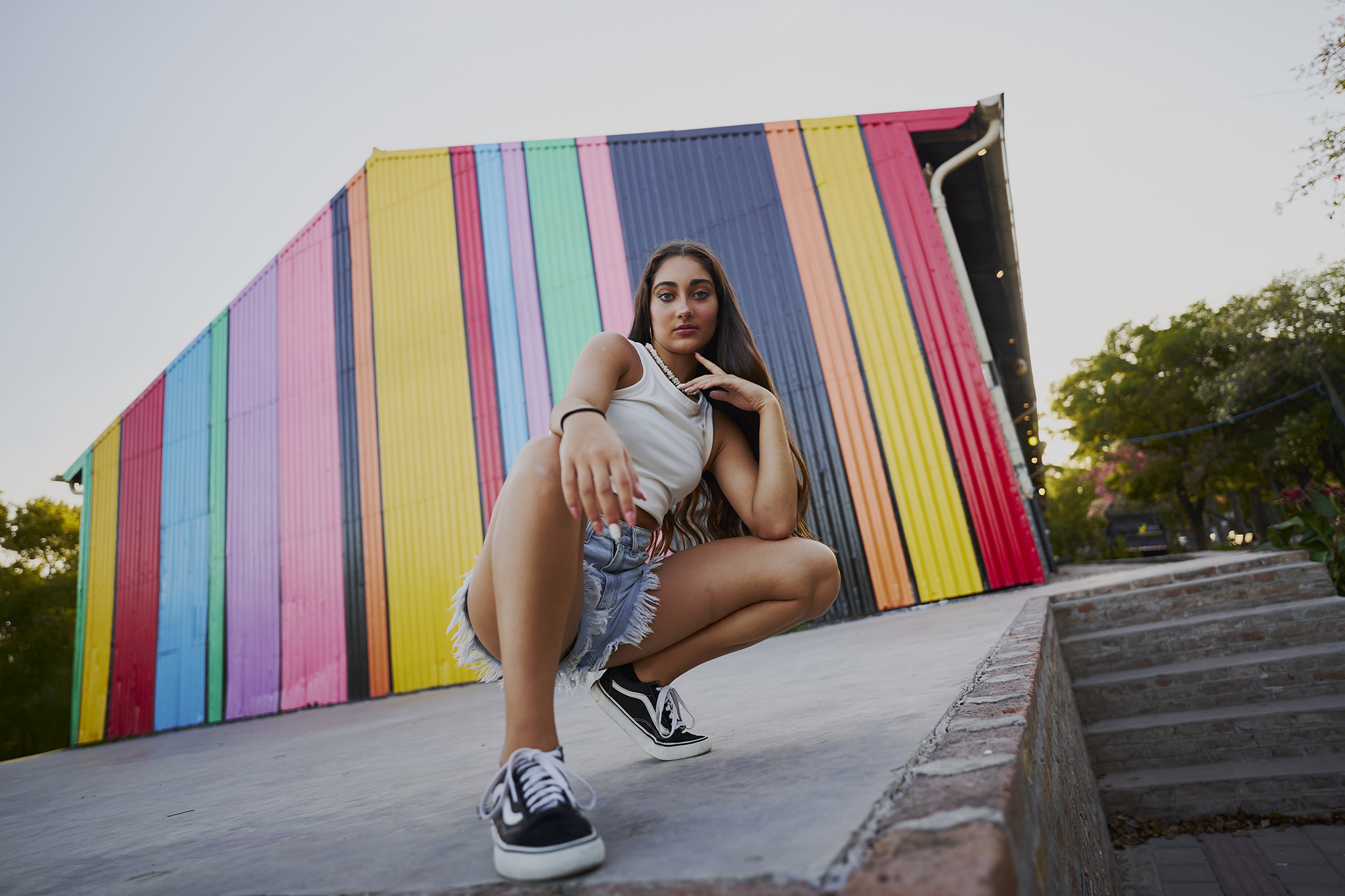 Pose en cuclillas frente a un muro de rayas de colores, en zapatillas. Book de quince urbano de DNX Estudio, San José 1672 Local 5, Funes.