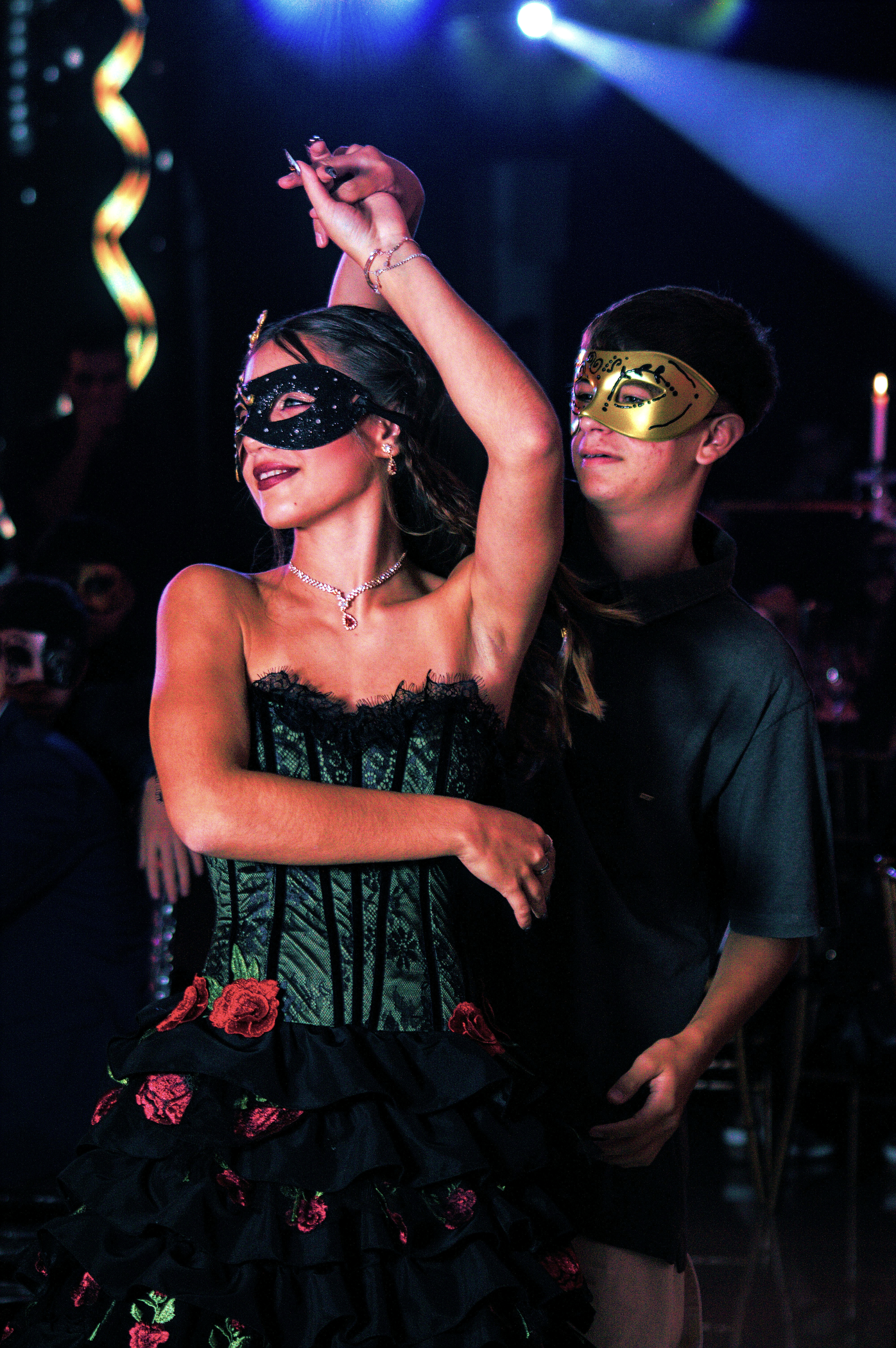 Quinceañera bailando con vestido gótico, con detalles en rojo y antifaz.